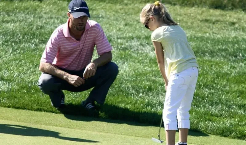 Jaime kneeling beside a junior golfer on the green